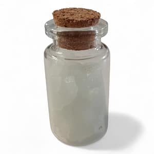 Botellita de cuarzo fosforescente sobre fondo blanco, con partículas luminosas que brillan en la oscuridad, ideal como amuleto espiritual