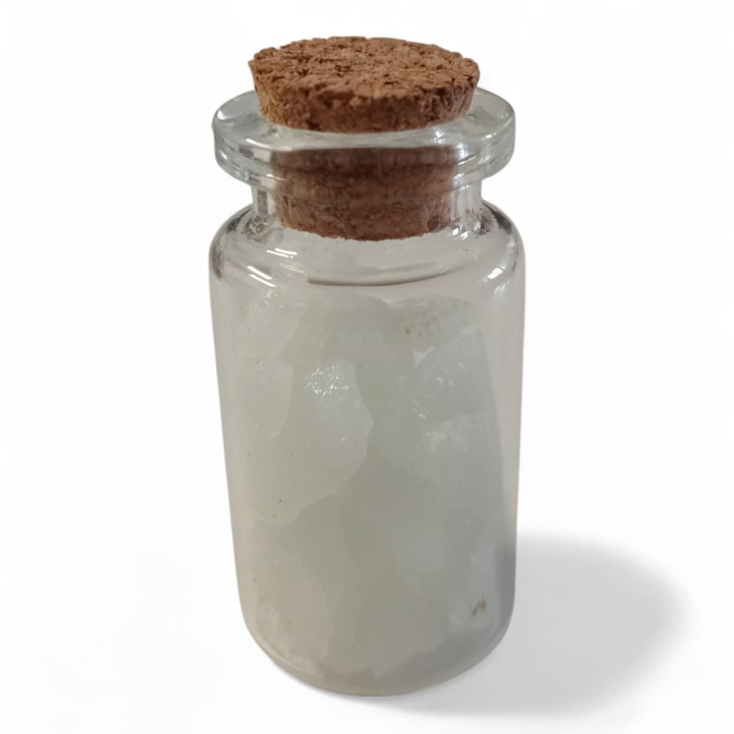 Botellita de cuarzo fosforescente sobre fondo blanco, con partículas luminosas que brillan en la oscuridad, ideal como amuleto espiritual